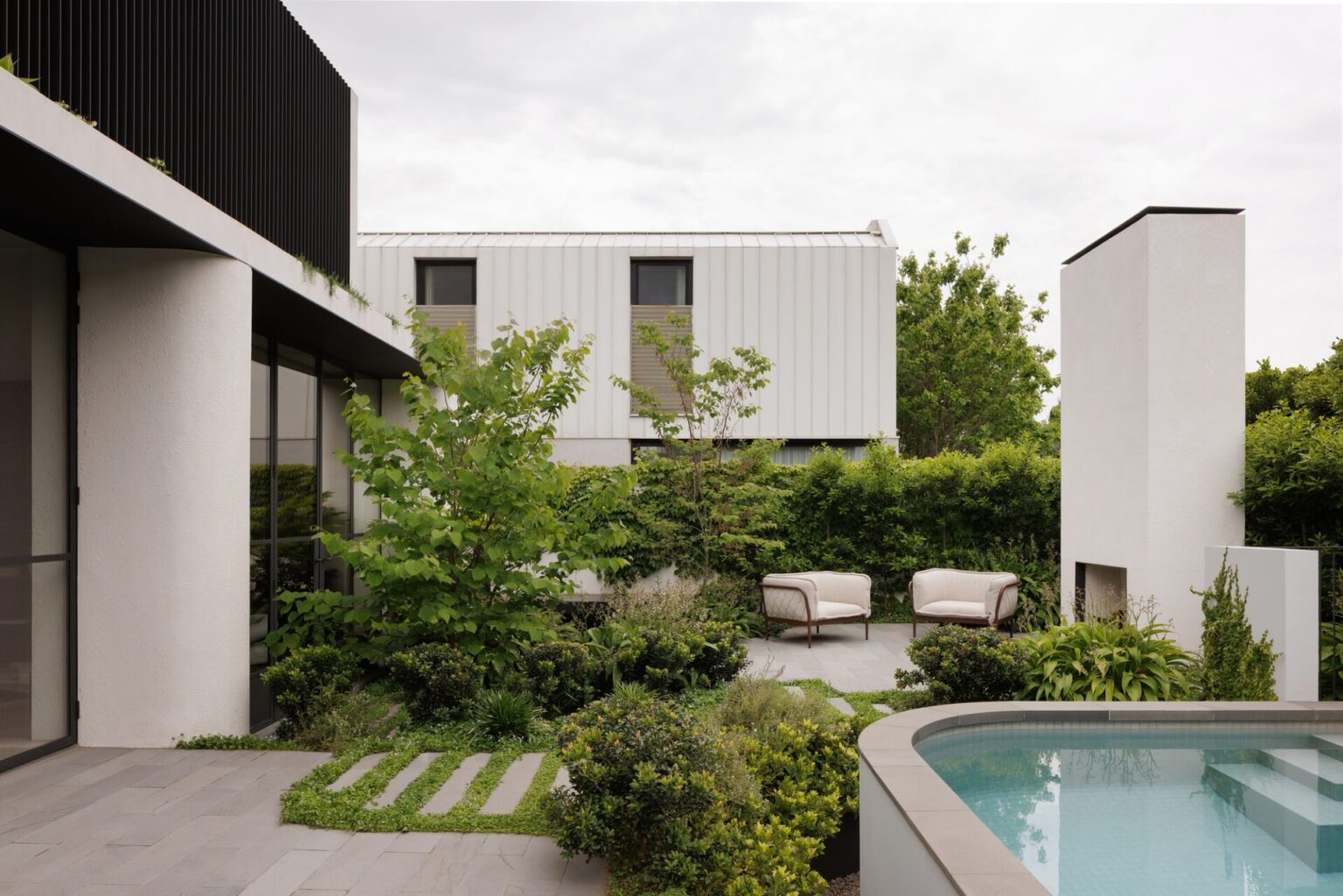 Modern backyard landscape construction in Melbourne featuring pool, concrete paving and architectural planting by Shape and Form.